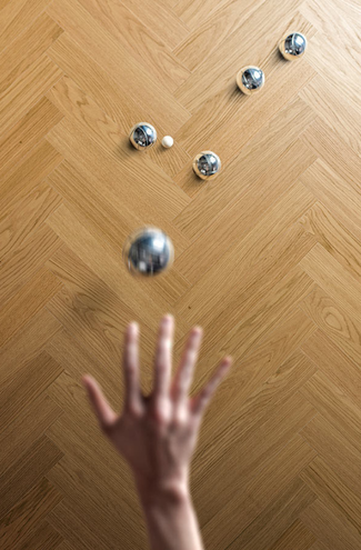 Image of a small hand throwing heavy metal balls onto a herringbone wood floor. Highest impact (dent & gouge) resistance. Outperforms traditional solid and engineered hardwood floors.